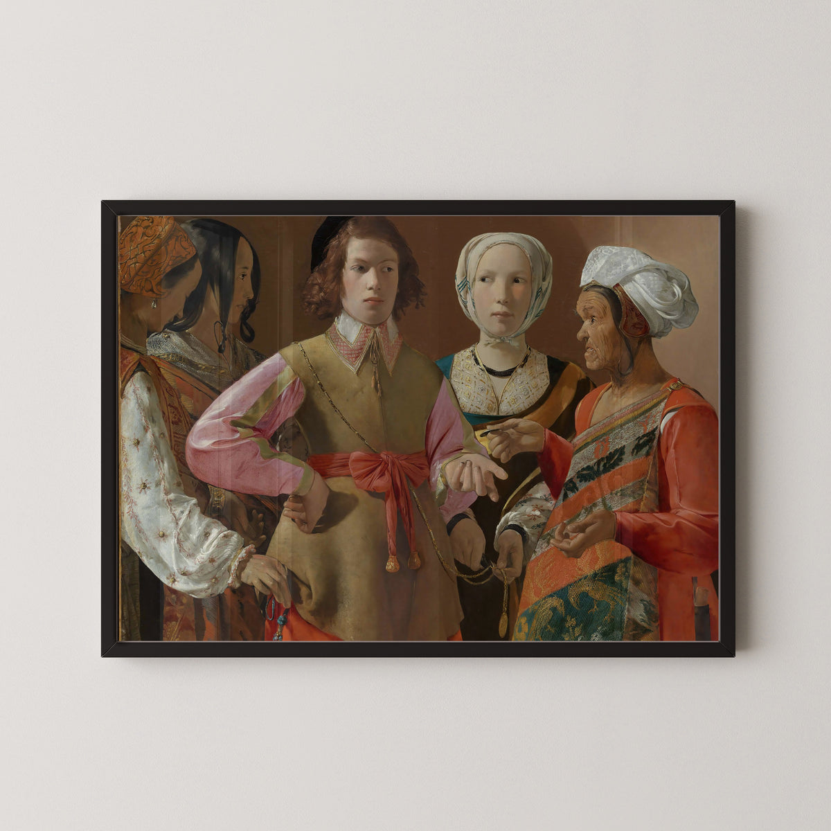 Framed art print of The Fortune-Teller by Georges de La Tour, in a black frame on a pale wall