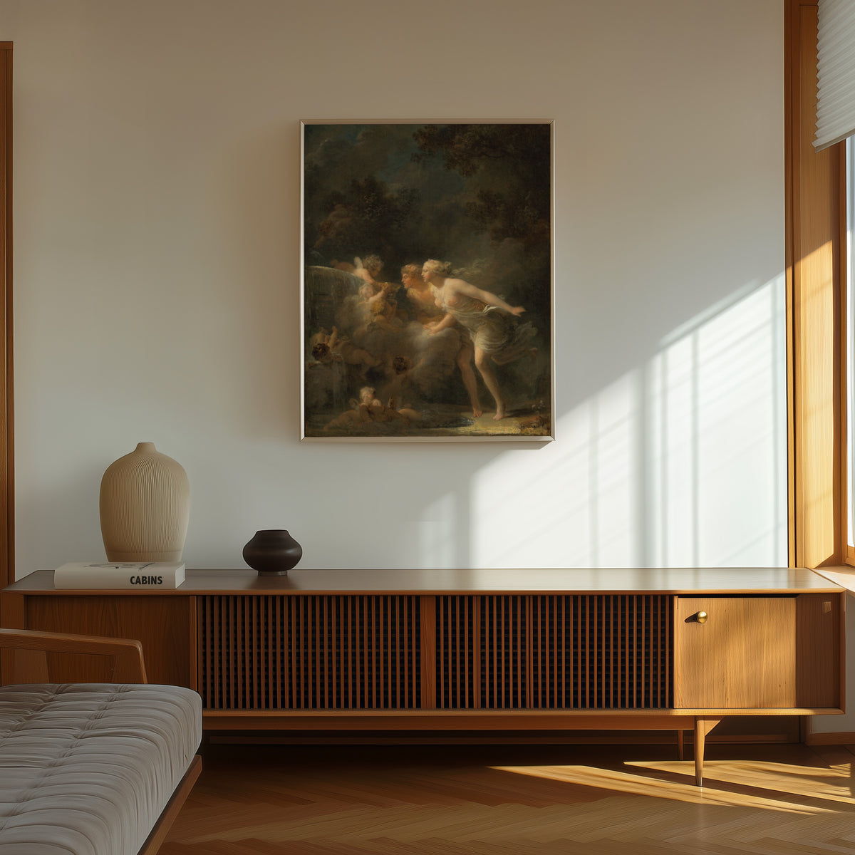 Framed art print of The Fountain of Love by Jean-Honoré Fragonard, in a thin light frame on a sunlit wall above a wooden sideboard