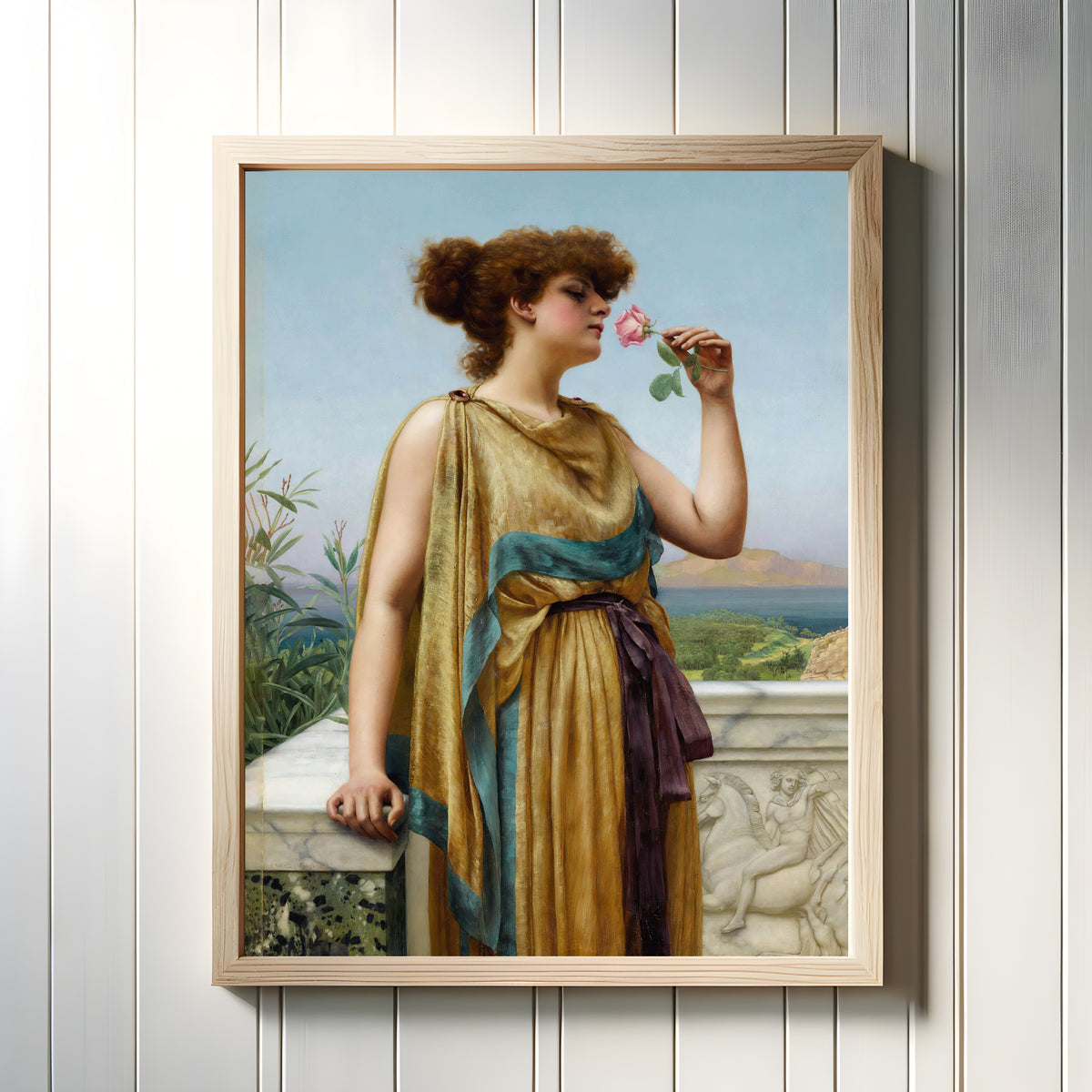 Framed art print of The Fragrant Rose by John William Godward, in a light wood frame on a white panelled wall