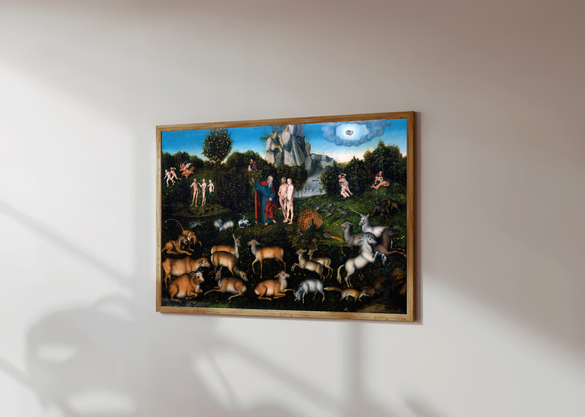 Framed art print of The Garden of Eden by Lucas Cranach the Elder, in a light wood frame on a sunlit white wall, seen at a slight angle