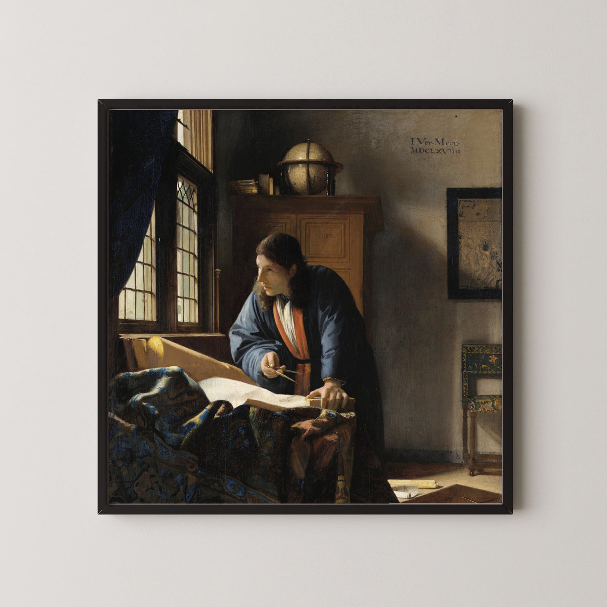 Framed art print of The Geographer by Johannes Vermeer, in a black frame on a pale wall