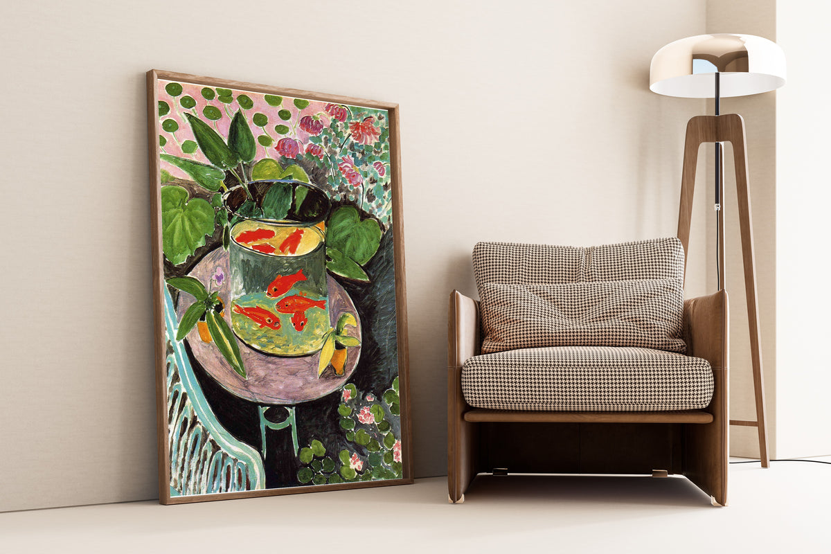 Framed art print of The Goldfish by Henri Matisse, leaning against a wall beside an armchair and a floor lamp