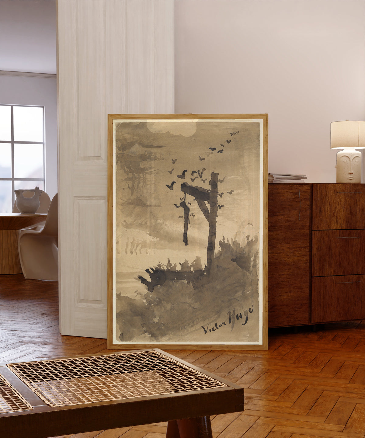 Framed art print of The Hanged Man by Victor Hugo, in a light wood frame leaning in a warm room with a parquet floor