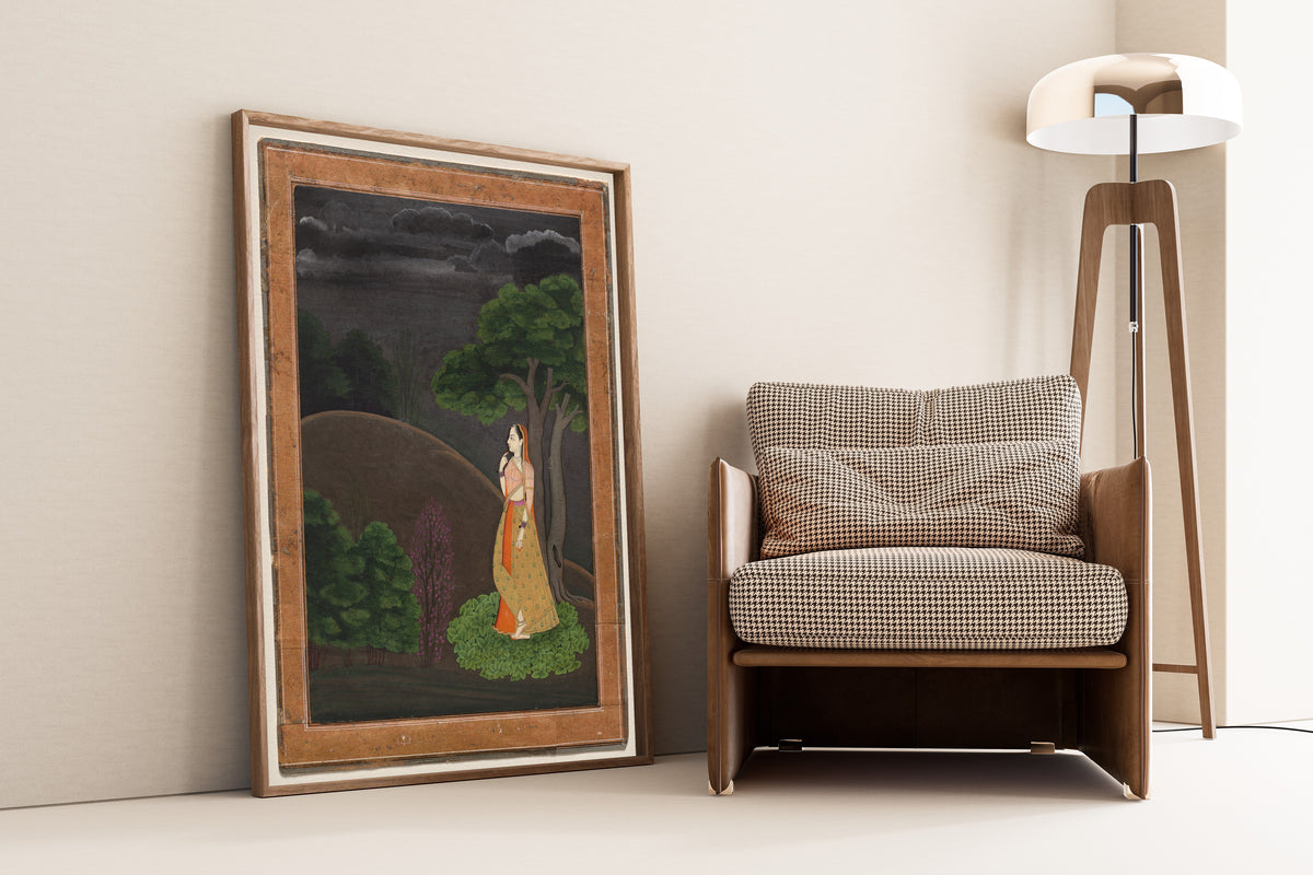 Framed art print of The Heroine Who Waits Anxiously for Her Absent Lover: Utka… by Pahari school, leaning against a wall beside an armchair and a floor lamp