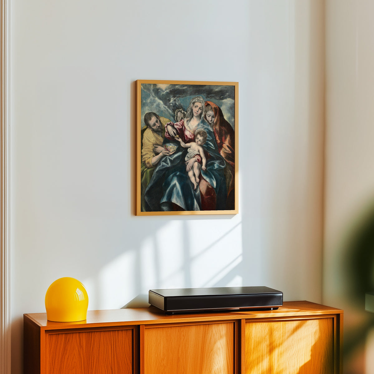 Framed art print of The Holy Family with Mary Magdalen by El Greco, in a light wood frame on a white wall above an orange sideboard