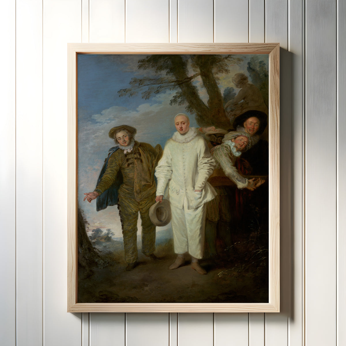 Framed art print of The Italian Comedians by Jean-Antoine Watteau, in a light wood frame on a white panelled wall