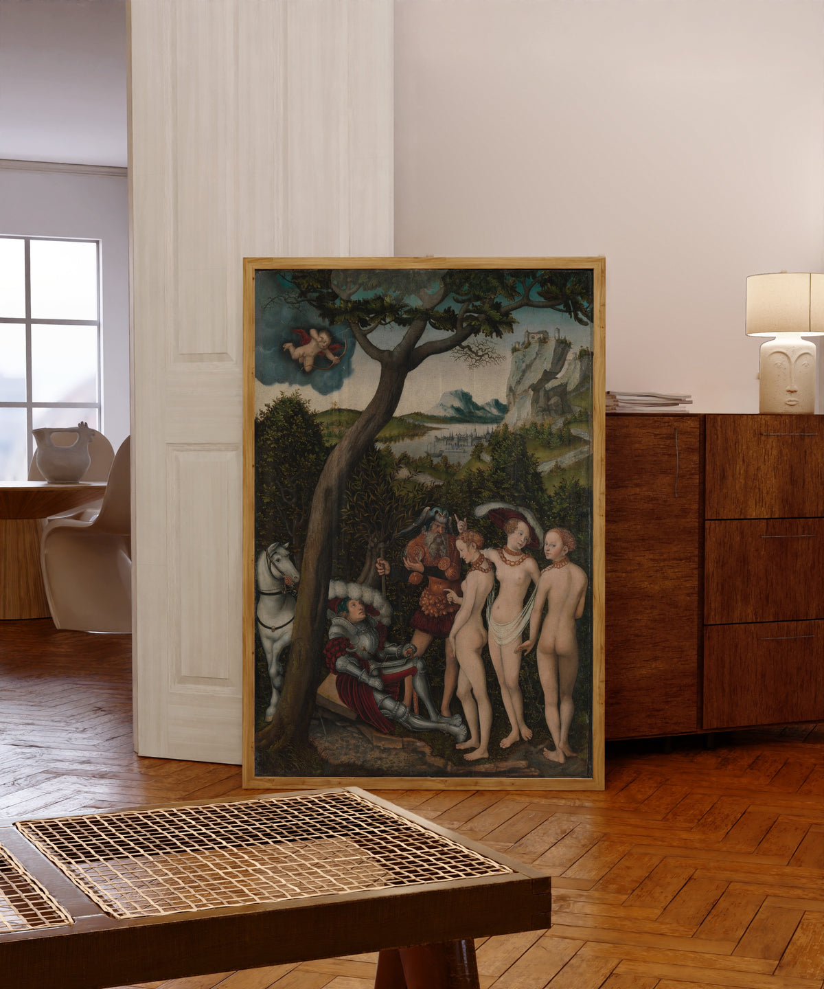 Framed art print of The Judgment of Paris by Lucas Cranach the Elder, in a light wood frame leaning in a warm room with a parquet floor