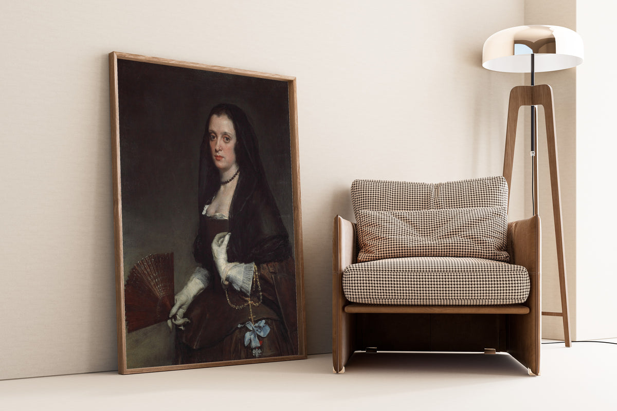 Framed art print of The Lady with a Fan by Diego Velázquez, leaning against a wall beside an armchair and a floor lamp