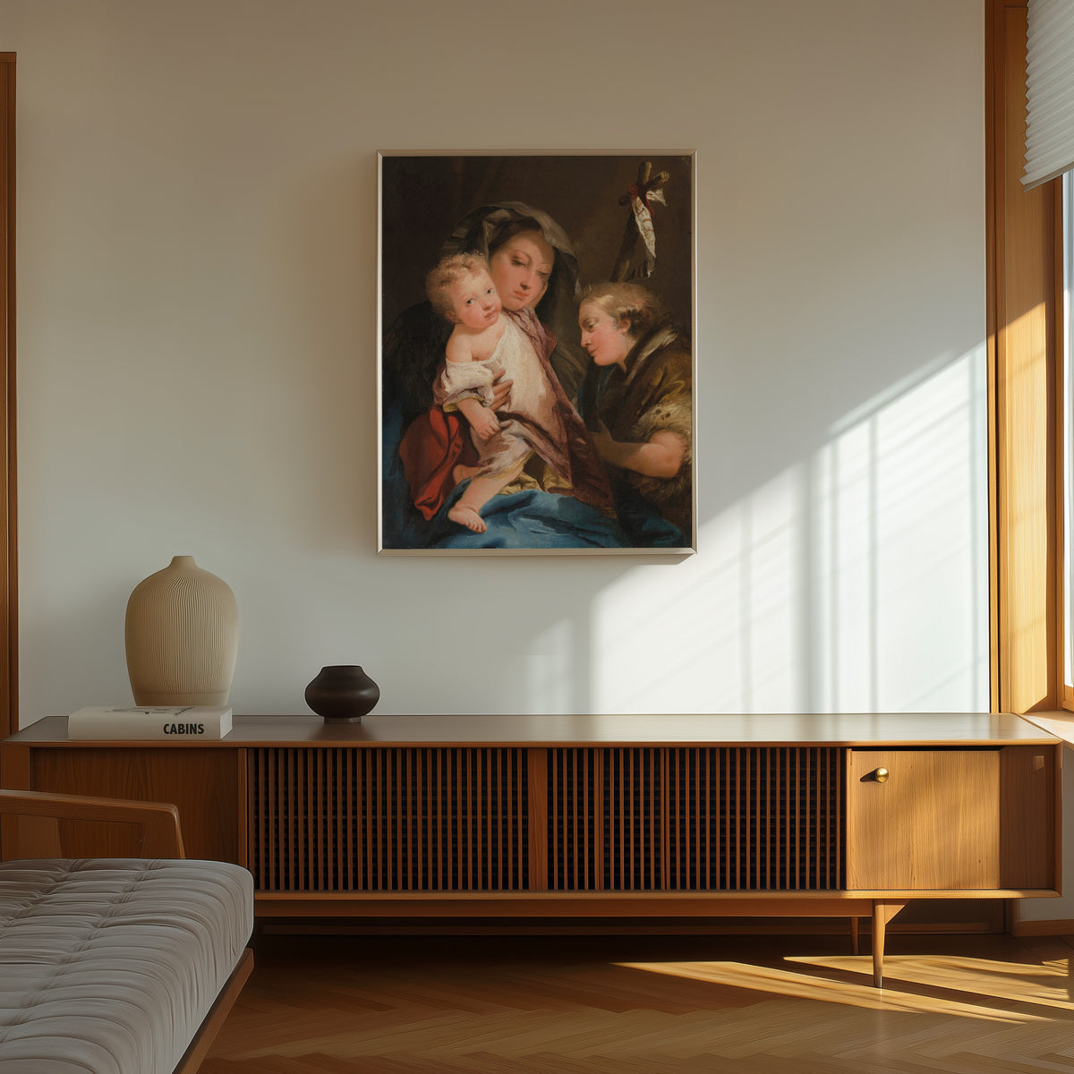 Framed art print of The Madonna and Child with the Infant Saint… by Giovanni Domenico Tiepolo, in a thin light frame on a sunlit wall above a wooden sideboard
