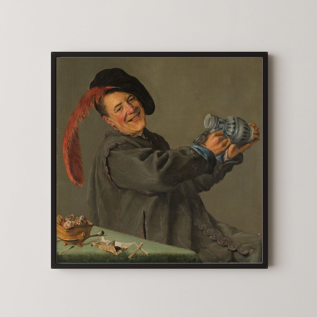 Framed art print of The Merry Drinker by Judith Leyster, in a black frame on a pale wall