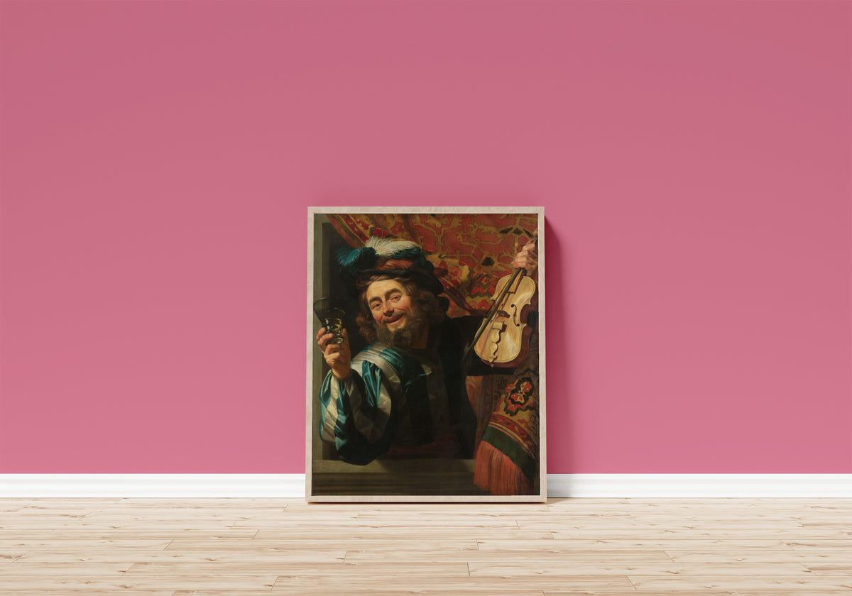 Framed art print of The Merry Fiddler by Gerrit van Honthorst, in a light wood frame leaning on a pink wall above a wooden floor