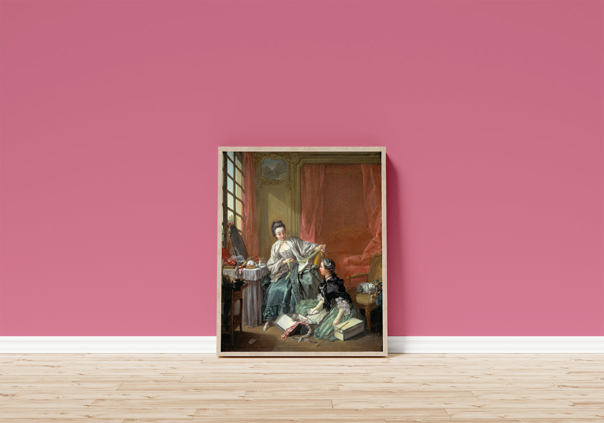Framed art print of The Milliner by François Boucher, in a light wood frame leaning on a pink wall above a wooden floor