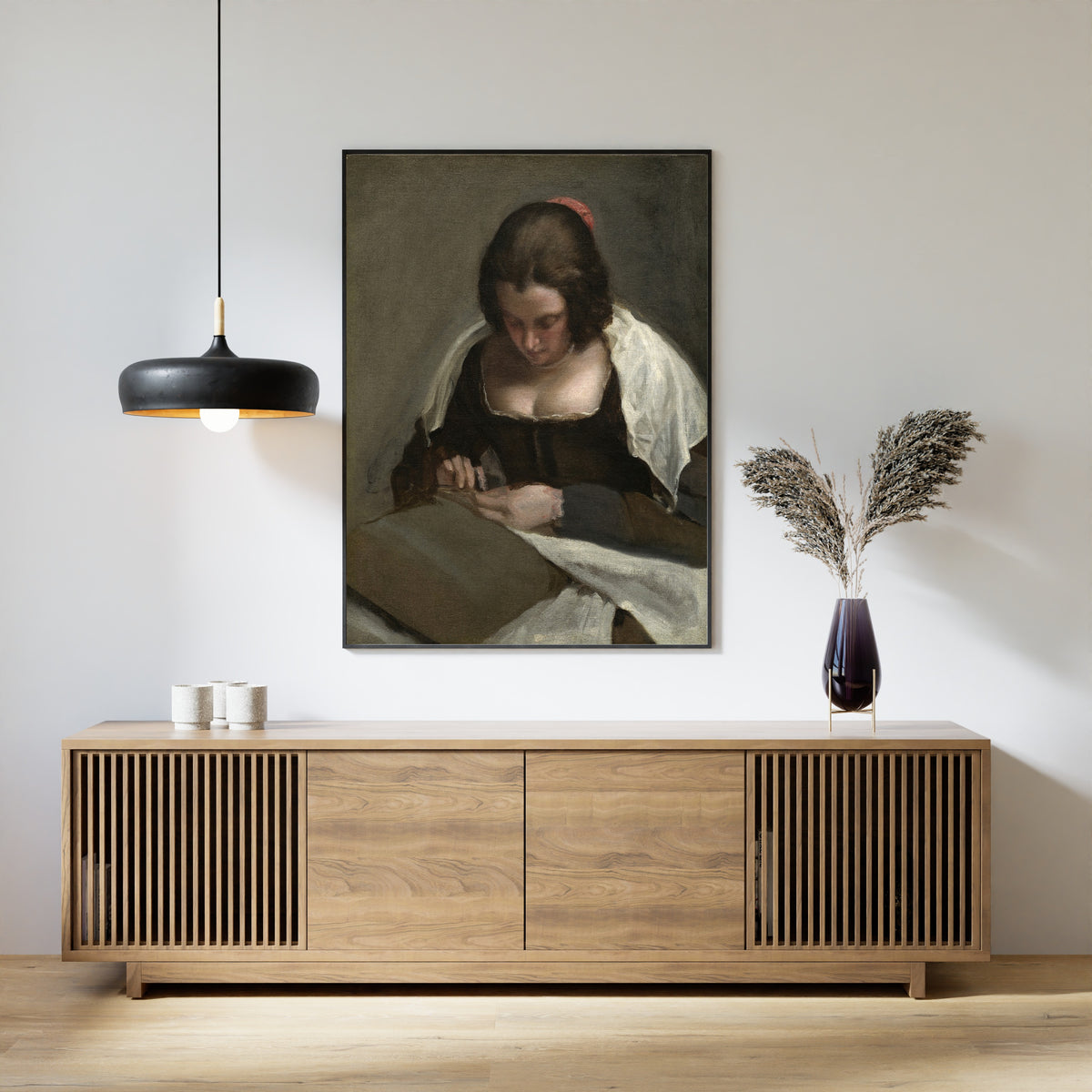 Framed art print of The Needlewoman by Diego Velázquez, above a slatted wood sideboard