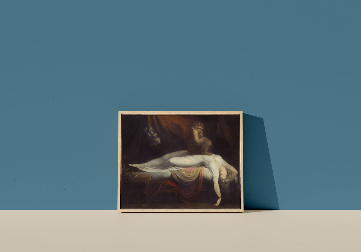 Framed art print of The Nightmare by Henry Fuseli, in a light wood frame leaning on a blue wall