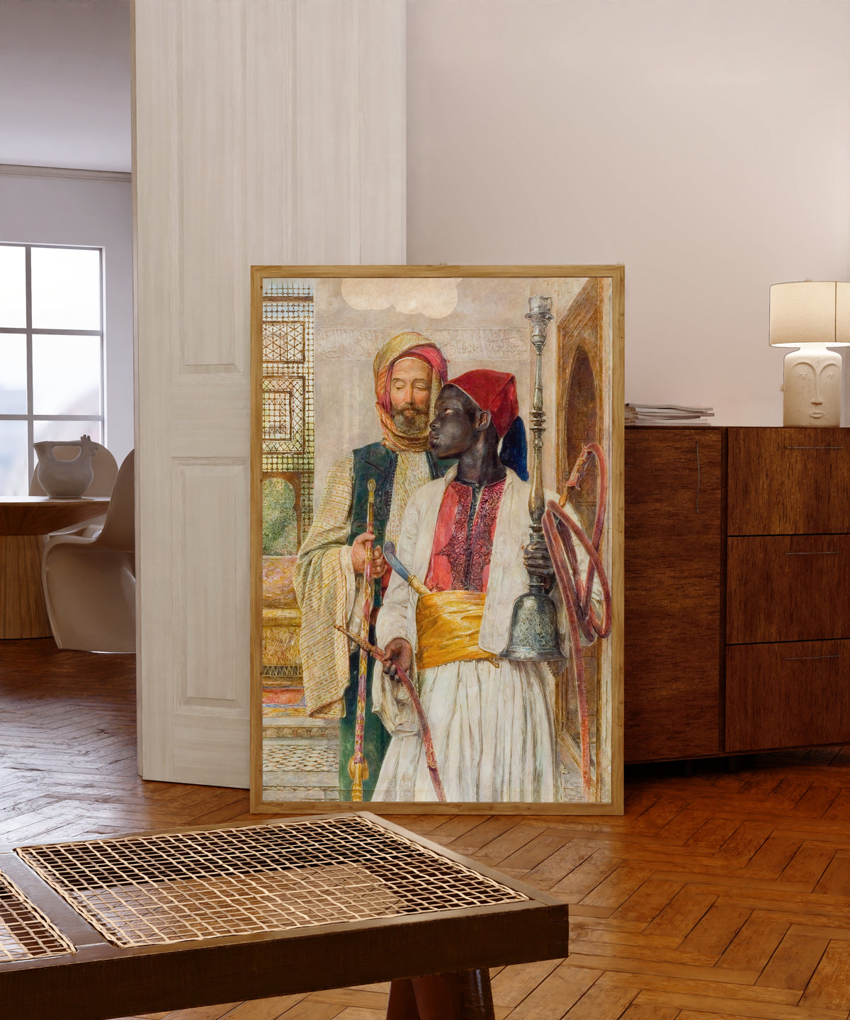 Framed art print of The Pipe Bearer by John Frederick Lewis, in a light wood frame leaning in a warm room with a parquet floor