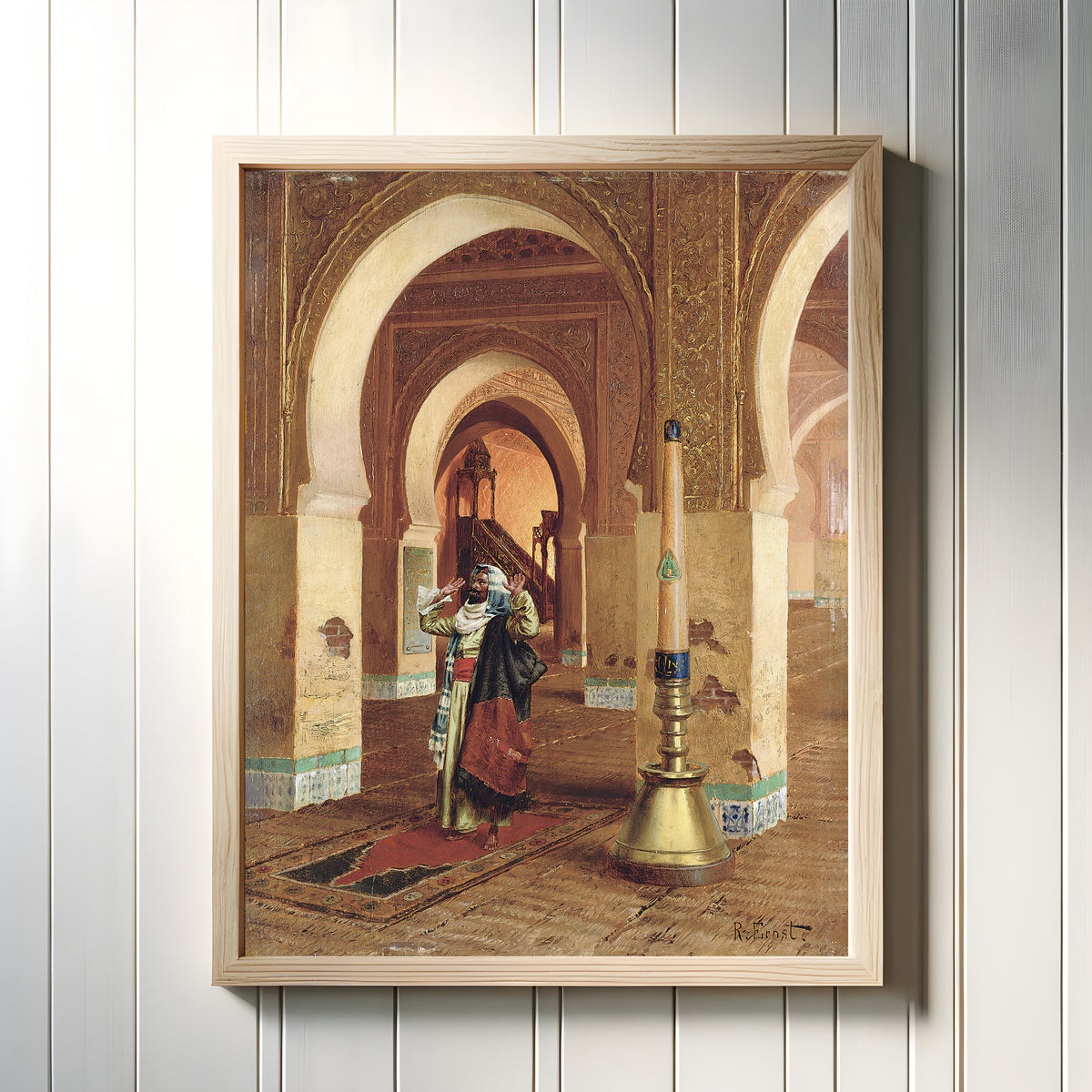 Framed art print of The Prayer by Rudolf Ernst, in a light wood frame on a white panelled wall