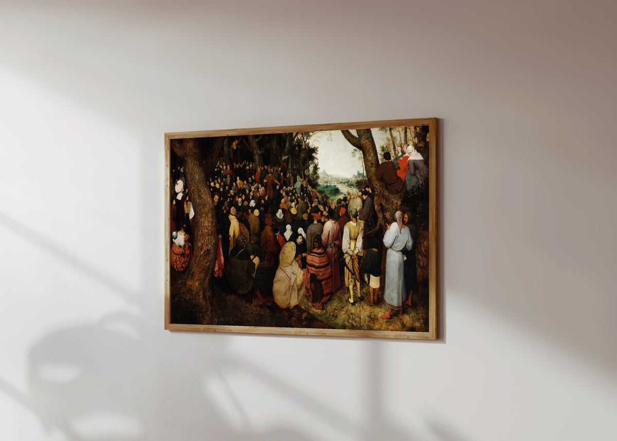 Framed art print of The Preaching of Saint John the Baptist by Pieter Bruegel the Elder, in a light wood frame on a sunlit white wall, seen at a slight angle