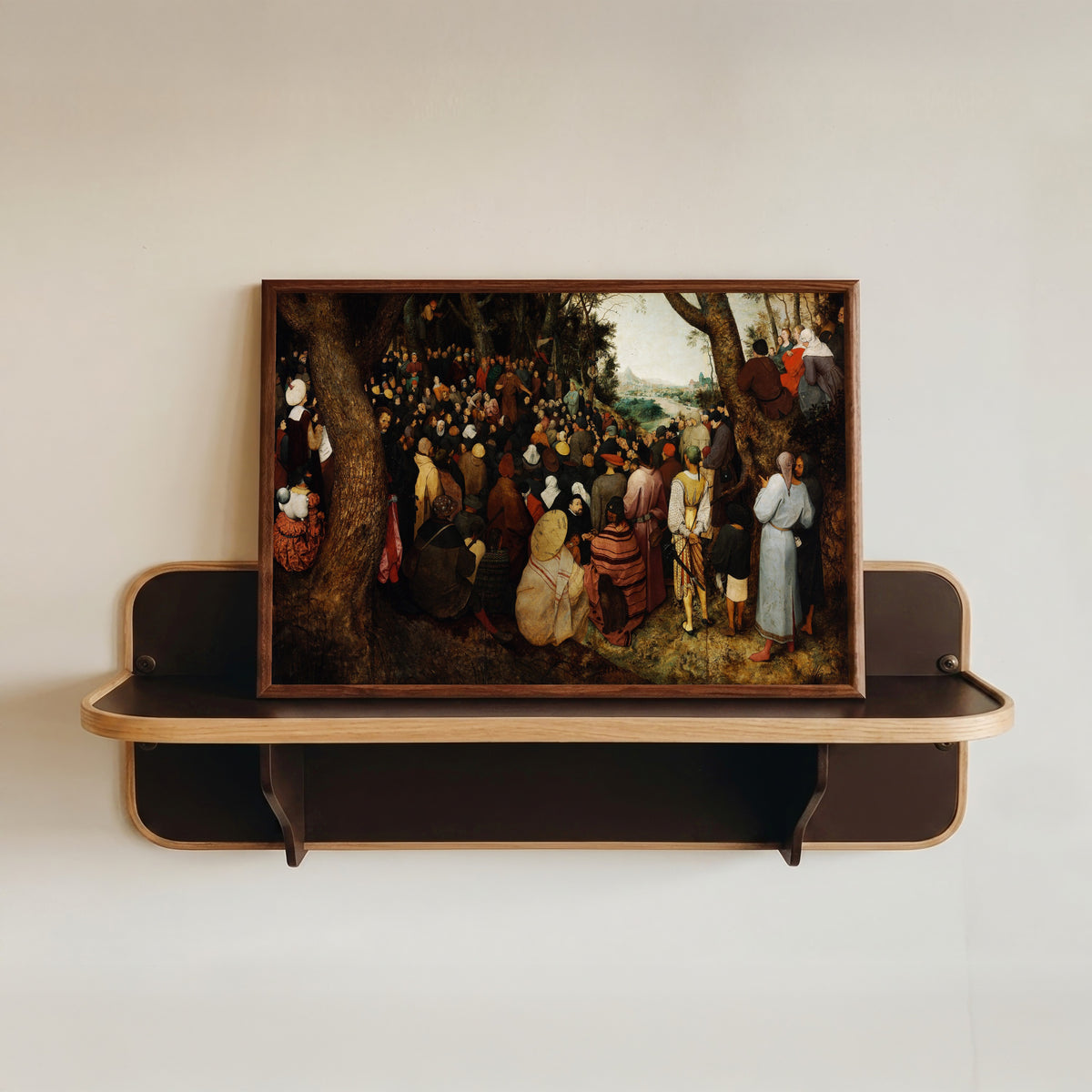 Framed art print of The Preaching of Saint John the Baptist by Pieter Bruegel the Elder, in a dark wood frame resting on a wall shelf