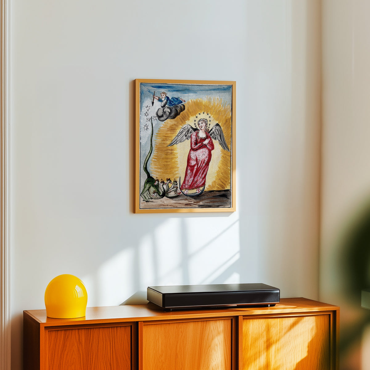 Framed art print of The Pregnant Virgin Mary with a Dragon at Her Feet by After Nicolas Flamel, in a light wood frame on a white wall above an orange sideboard