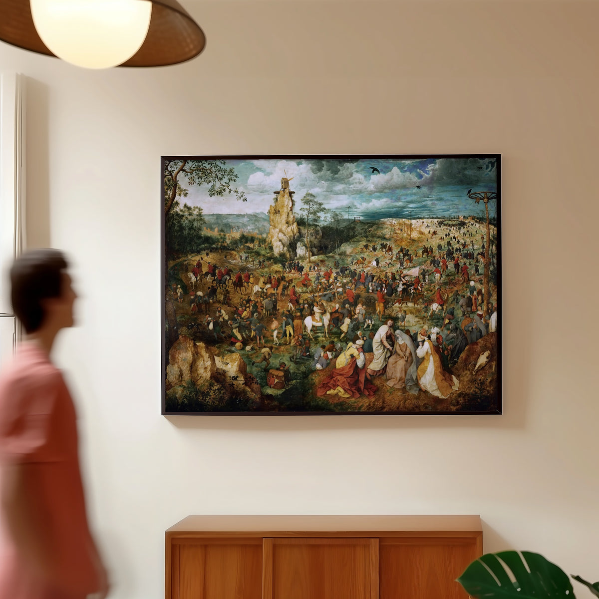 Framed art print of The Procession to Calvary by Pieter Bruegel the Elder, in a slim black frame on a warm wall in a sunlit room