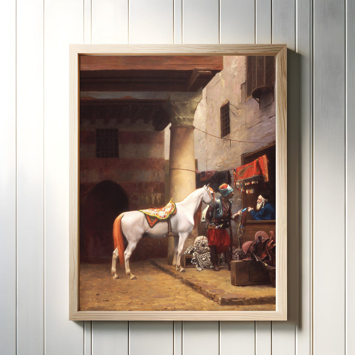 Framed art print of The Saddle Bazaar, Cairo by Jean-Léon Gérôme, in a light wood frame on a white panelled wall