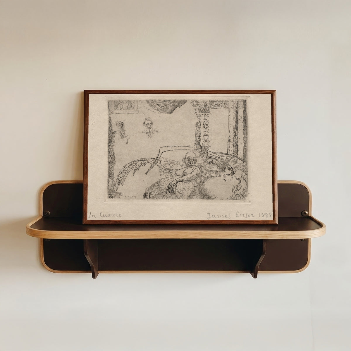 Framed art print of The Seven Deadly Sins: Lust by James Ensor, in a dark wood frame resting on a wall shelf
