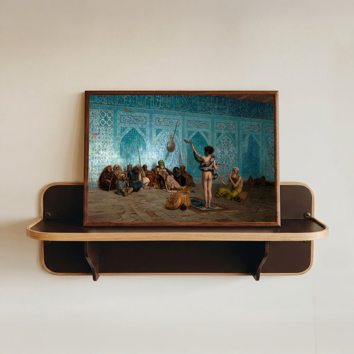 Framed art print of The Snake Charmer by Jean-Léon Gérôme, in a dark wood frame resting on a wall shelf