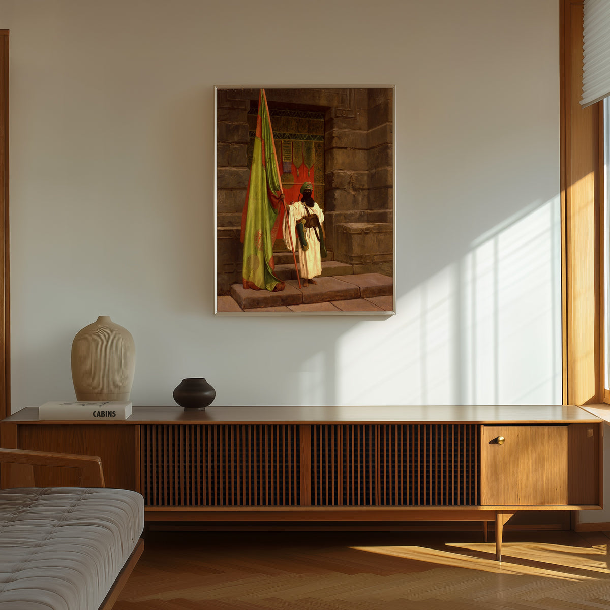 Framed art print of The Standing Bearer, Unfolding the Holy Flag by Jean-Léon Gérôme, in a thin light frame on a sunlit wall above a wooden sideboard