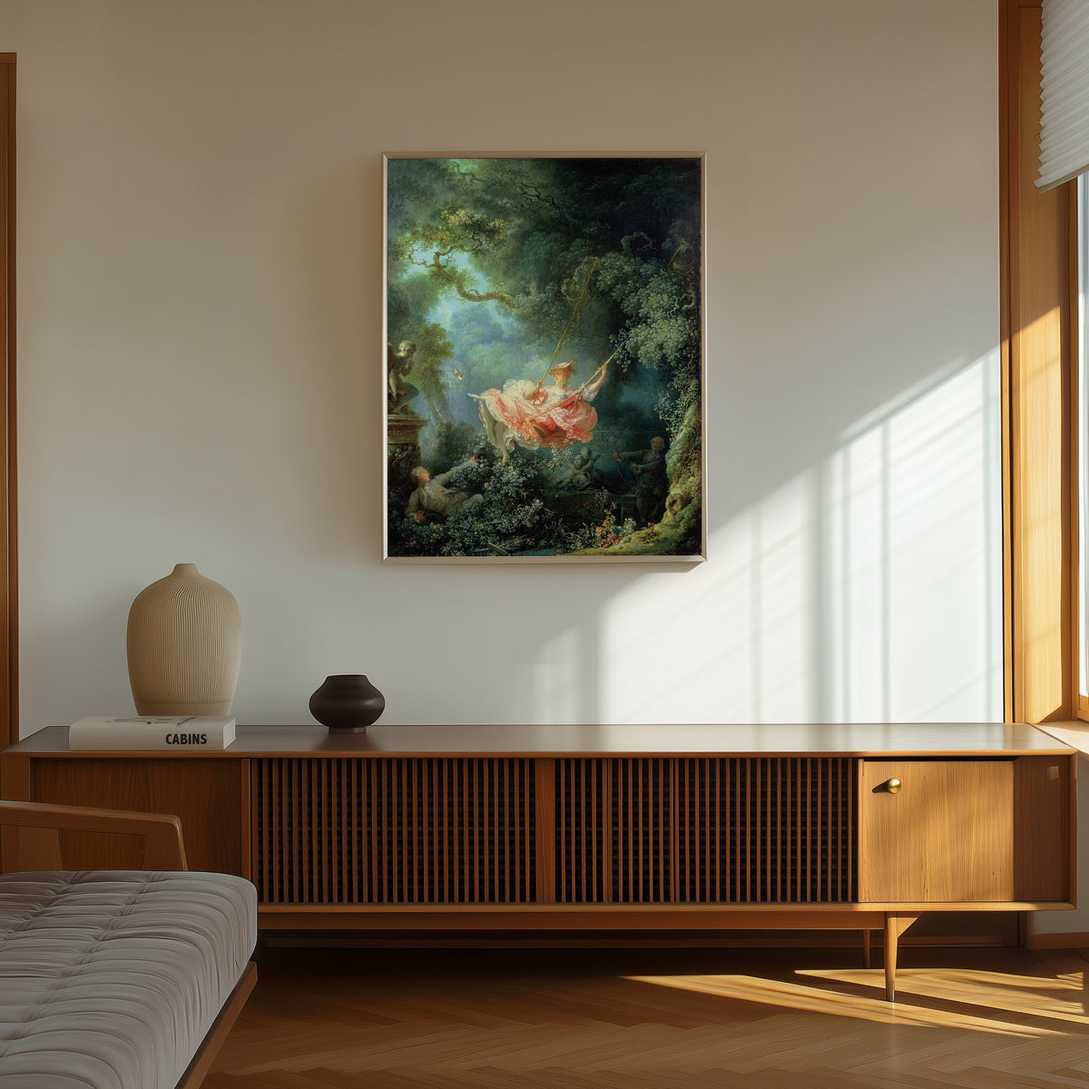 Framed art print of The Swing by Jean-Honoré Fragonard, in a thin light frame on a sunlit wall above a wooden sideboard