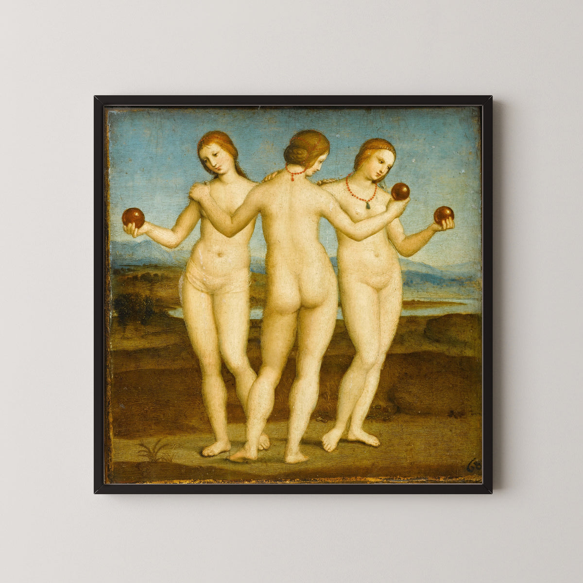 Framed art print of The Three Graces by Raphael, in a black frame on a pale wall