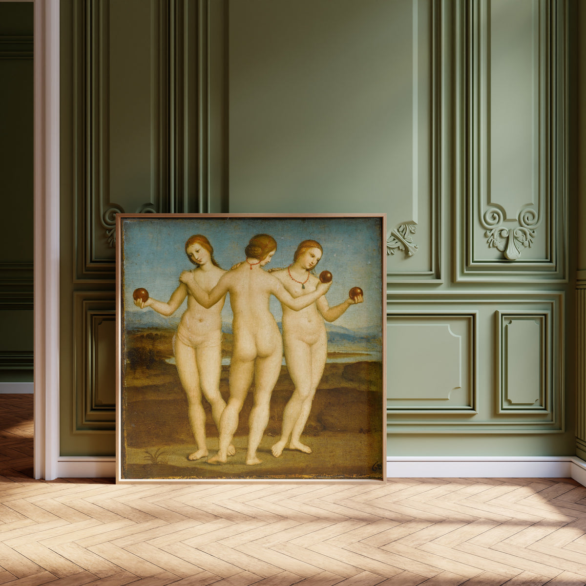 Framed art print of The Three Graces by Raphael, leaning against olive-green panelling on a herringbone floor