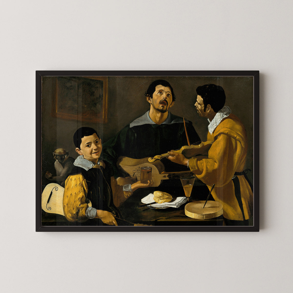 Framed art print of The Three Musicians by Diego Velázquez, in a black frame on a pale wall