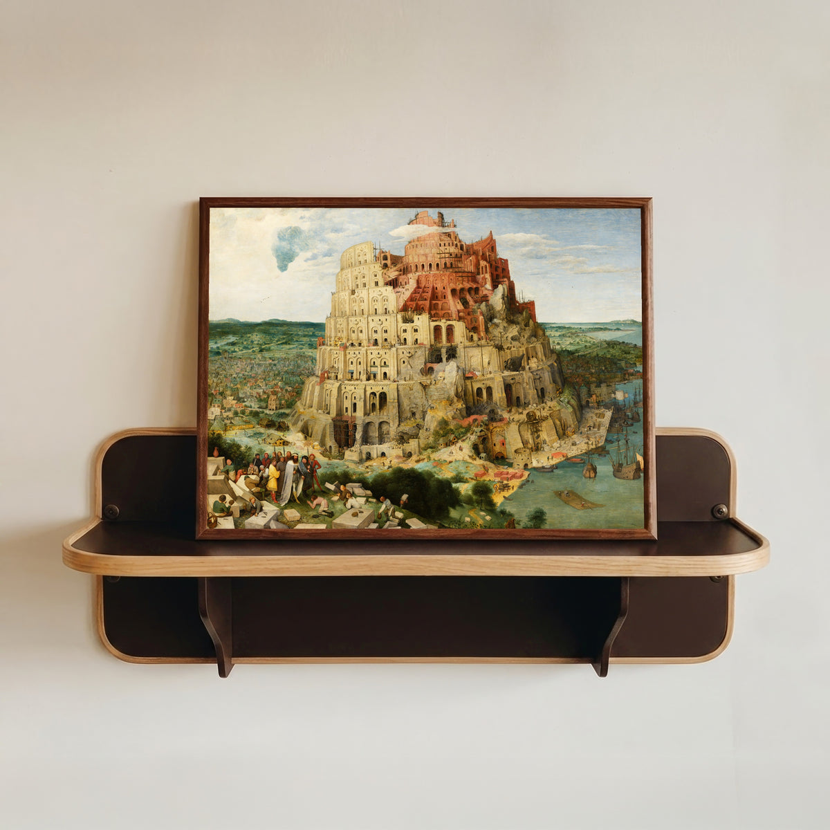 Framed art print of The Tower of Babel (Vienna) by Pieter Bruegel the Elder, in a dark wood frame resting on a wall shelf