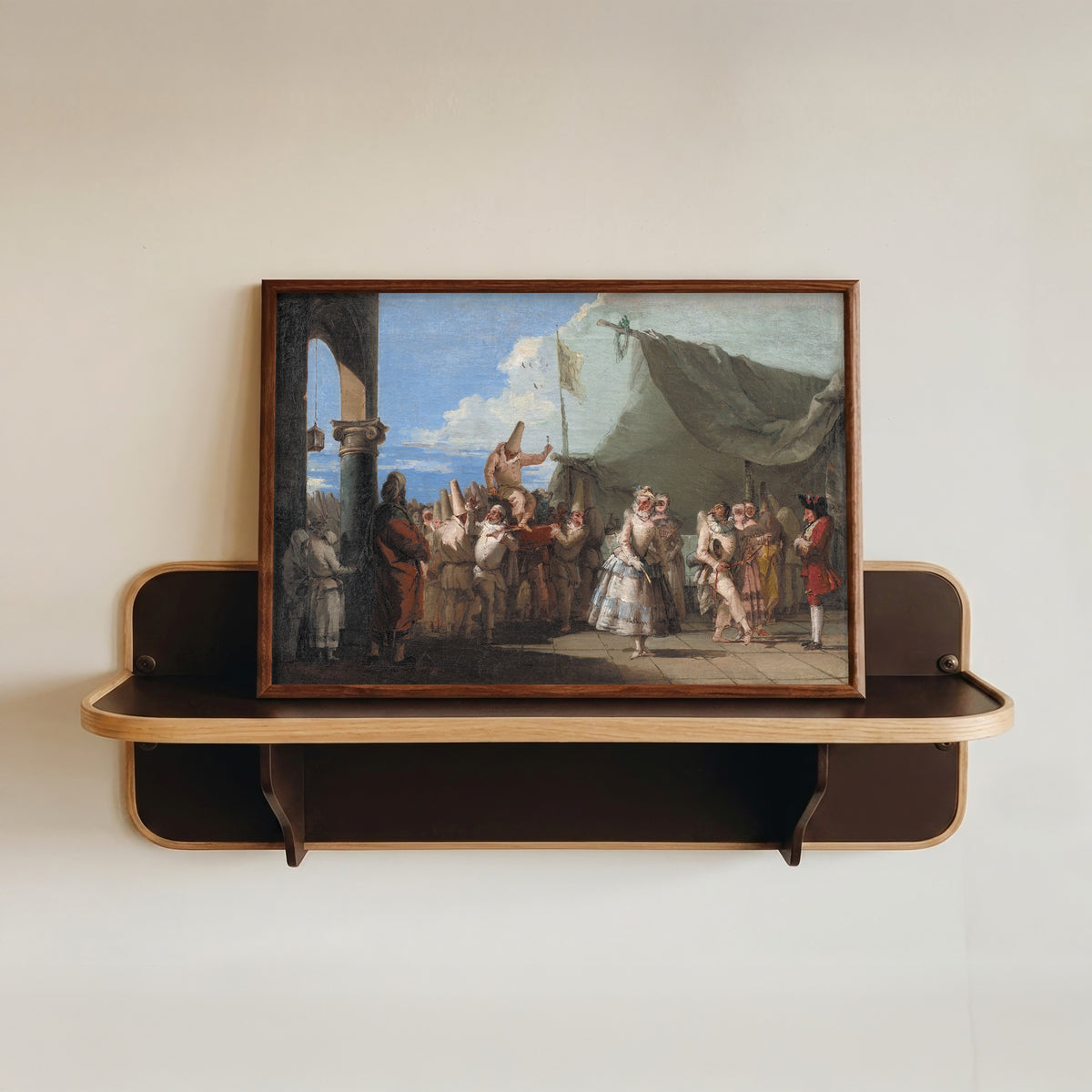 Framed art print of The Triumph of Pulcinella by Giovanni Domenico Tiepolo, in a dark wood frame resting on a wall shelf
