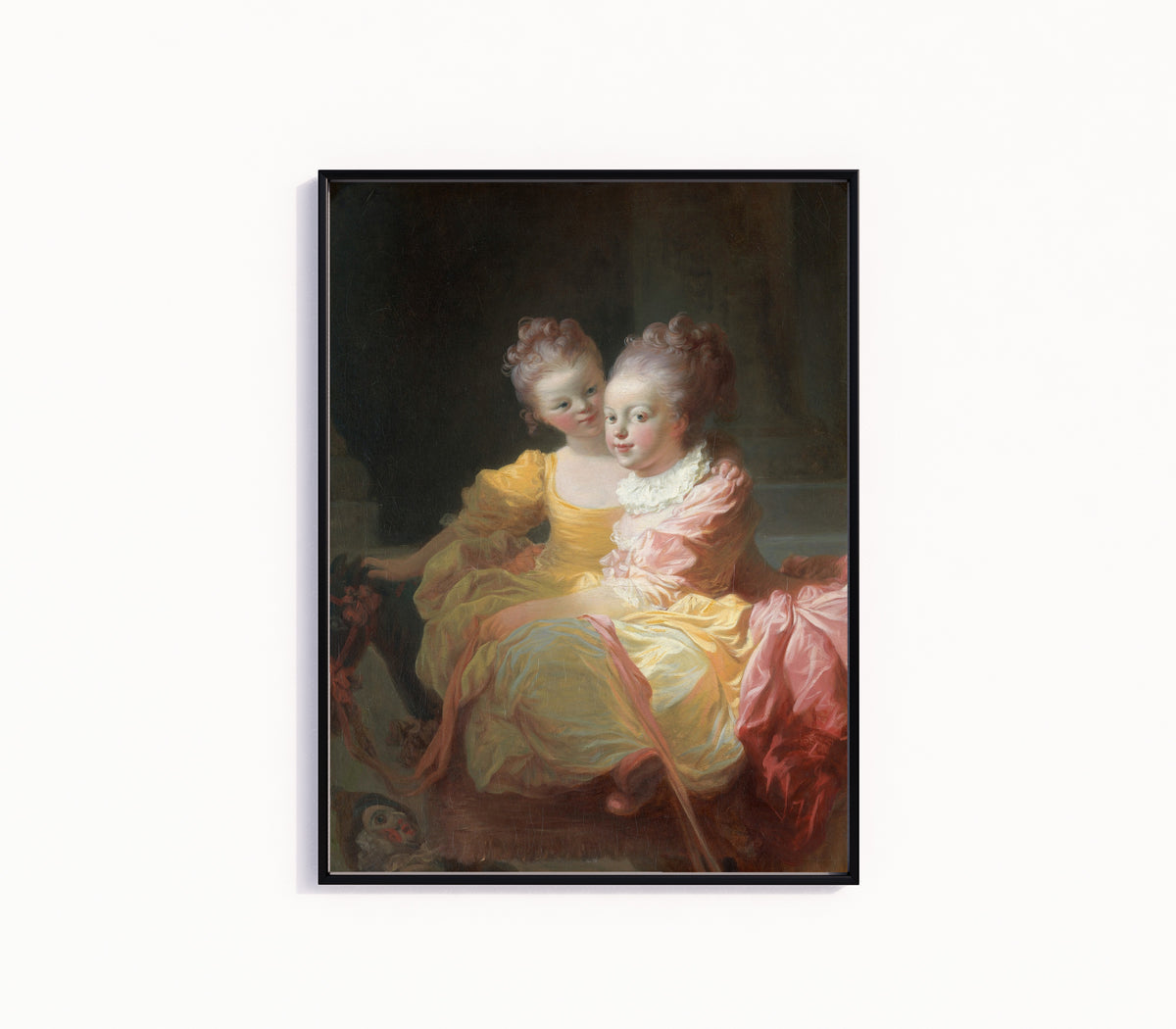 Framed art print of The Two Sisters by Jean-Honoré Fragonard, in a slim black frame on a plain white wall