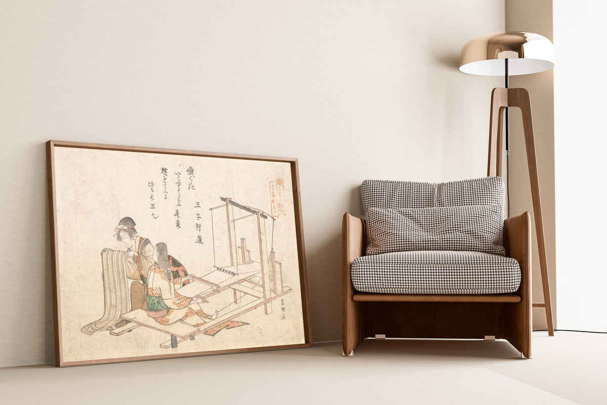Framed art print of The Weaving Factory by Katsushika Hokusai, leaning against a wall beside an armchair and a floor lamp