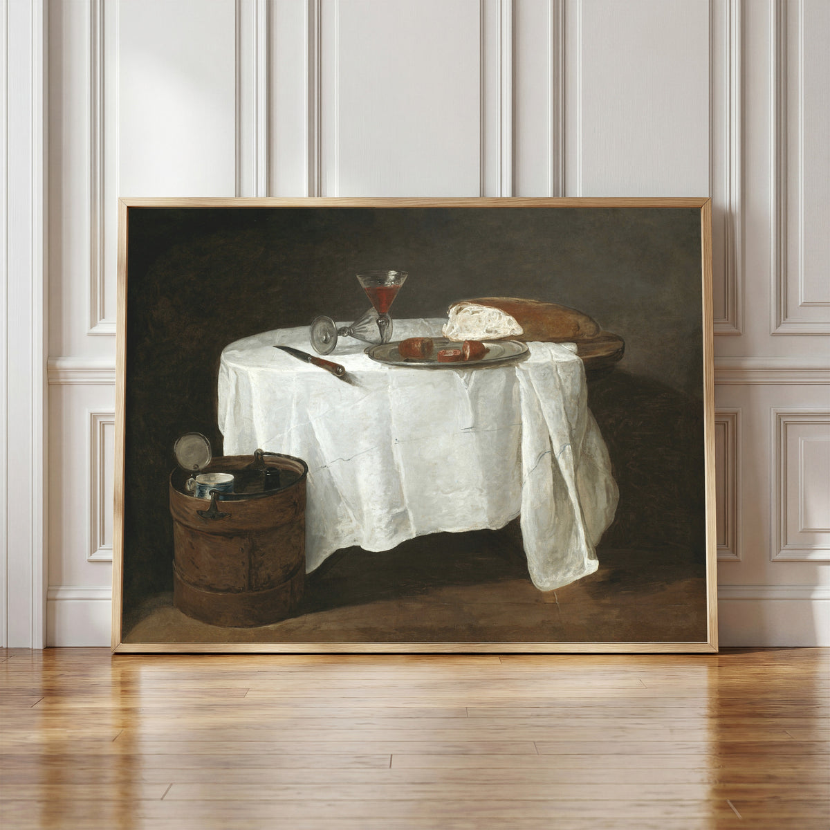 Framed art print of The White Tablecloth by Jean-Siméon Chardin, in a light wood frame leaning against a panelled white wall