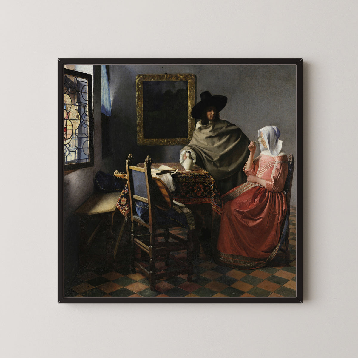 Framed art print of The Wine Glass by Johannes Vermeer, in a black frame on a pale wall