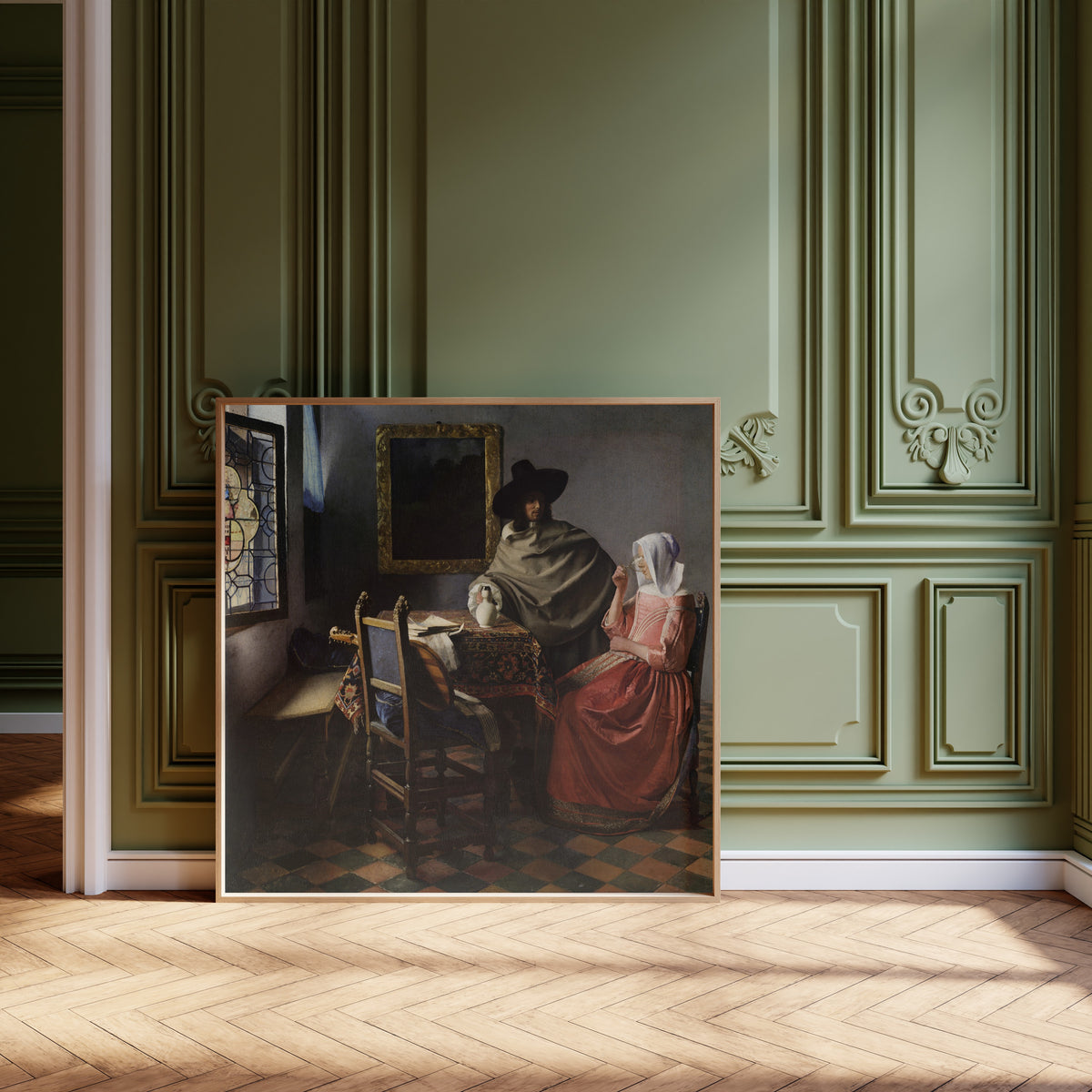Framed art print of The Wine Glass by Johannes Vermeer, leaning against olive-green panelling on a herringbone floor