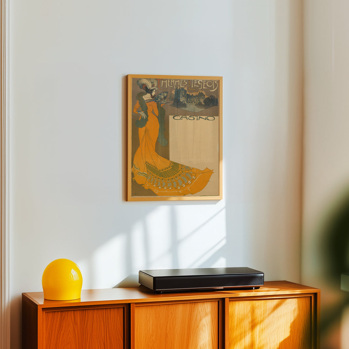 Framed art print of Thermes Liégeois Casino by Georges de Feure, in a light wood frame on a white wall above an orange sideboard