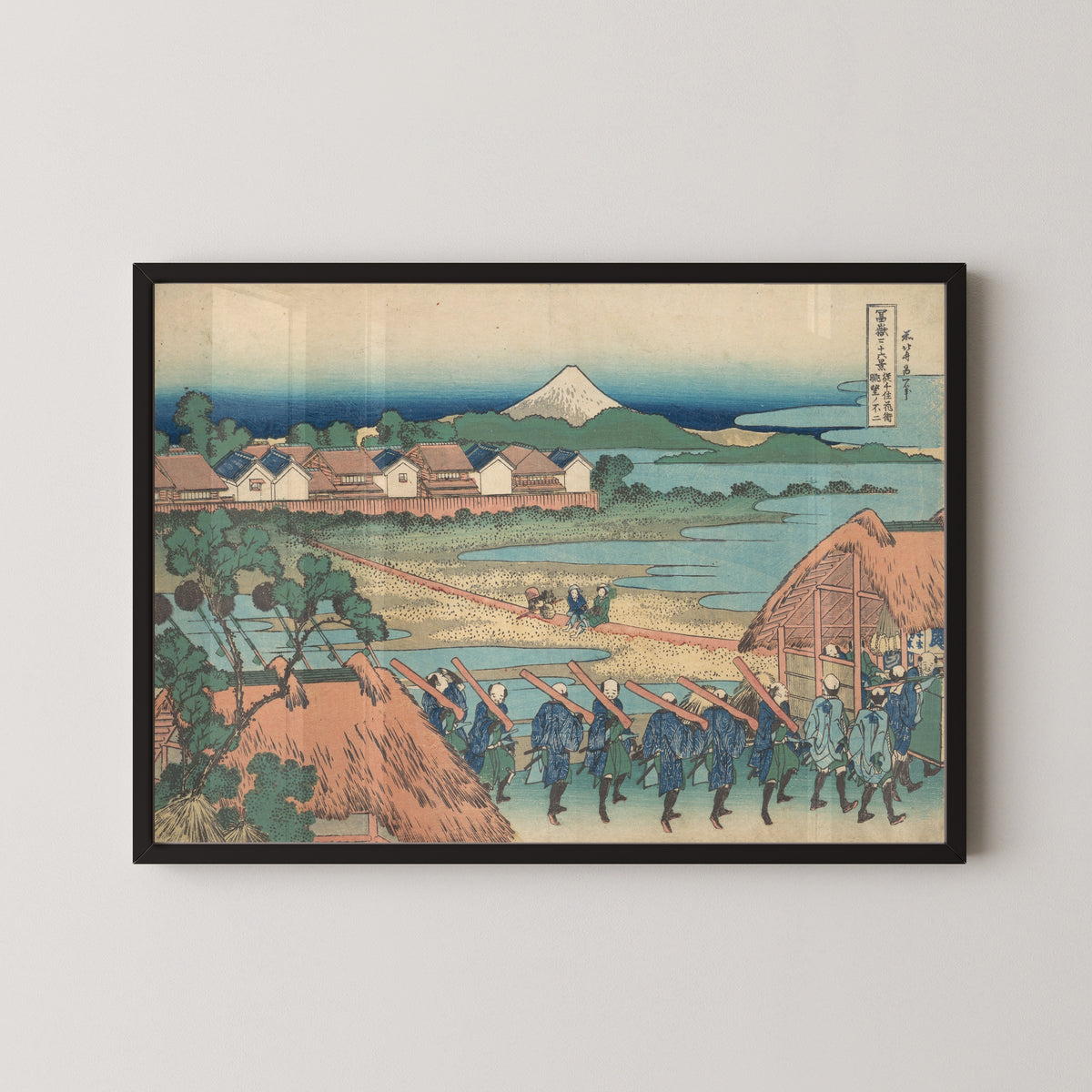 Framed art print of Thirty-six Views of Mount Fuji: Fuji Seen in the Distance from Senju Pleasure Quarter by Katsushika Hokusai, in a black frame on a pale wall