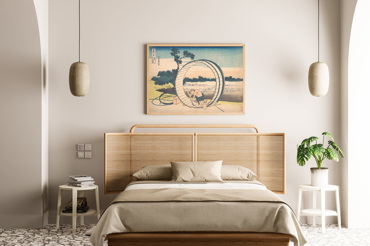 Framed art print of Thirty-six Views of Mount Fuji: Fujimigahara in Owari Province by Katsushika Hokusai, above a cane-headboard bed
