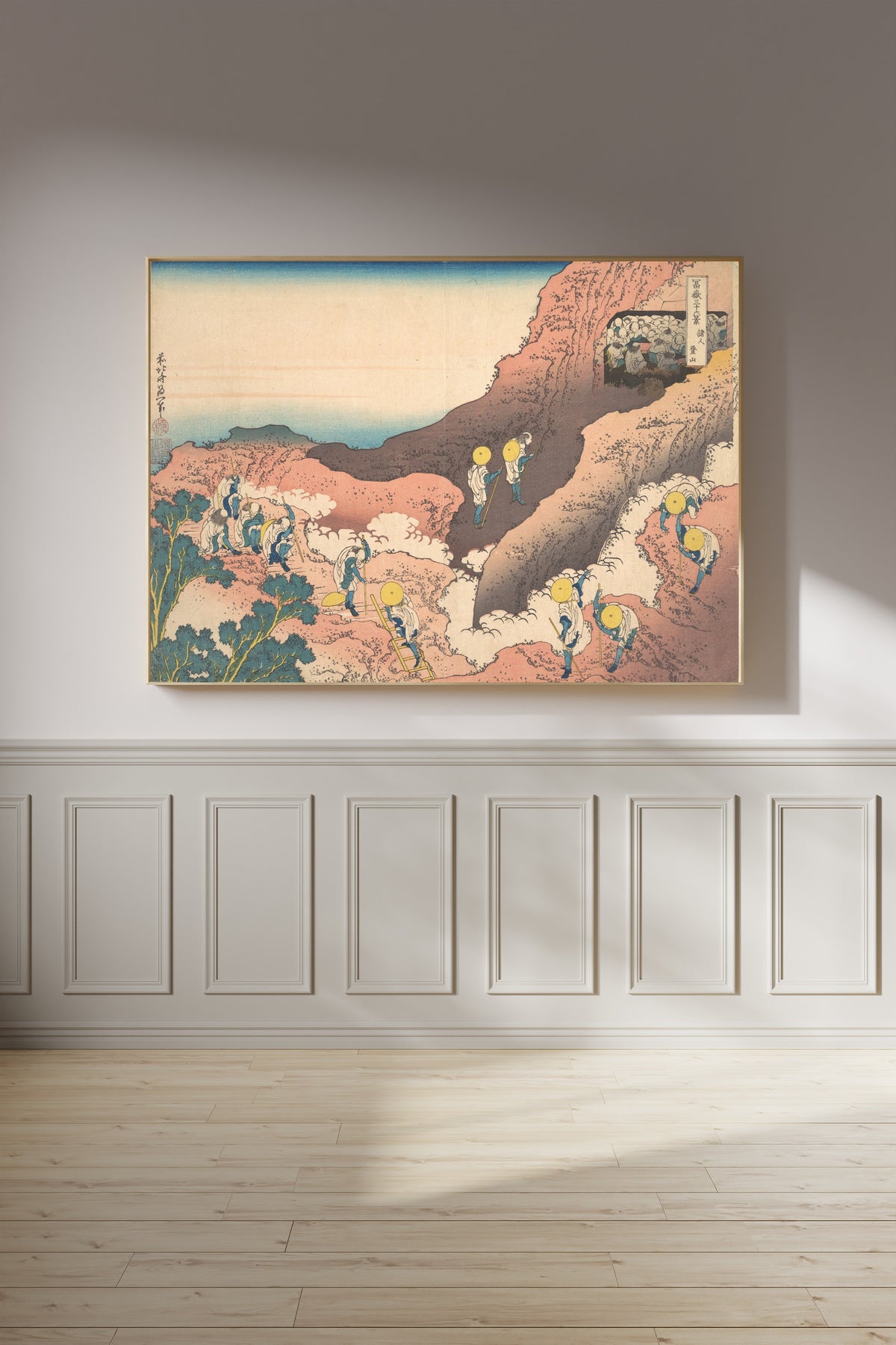 Framed art print of Thirty-six Views of Mount Fuji: Groups of Mountain Climbers by Katsushika Hokusai, on a panelled wall in afternoon light