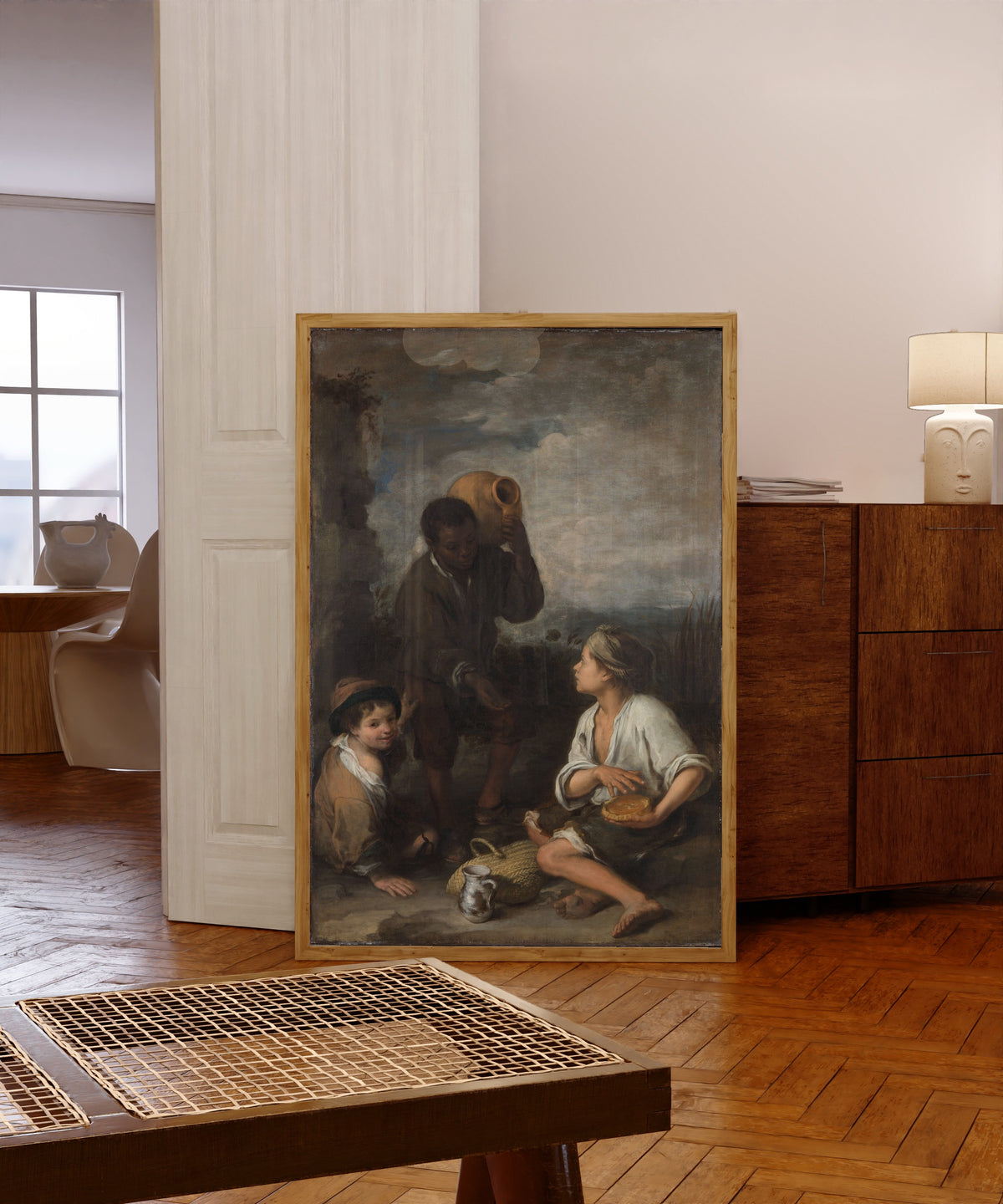 Framed art print of Three Boys by Bartolomé Esteban Murillo, in a light wood frame leaning in a warm room with a parquet floor
