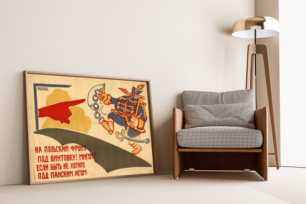 Framed art print of To the Polish Front, Under the Rifle! At Once! by Vladimir Mayakovsky, leaning against a wall beside an armchair and a floor lamp