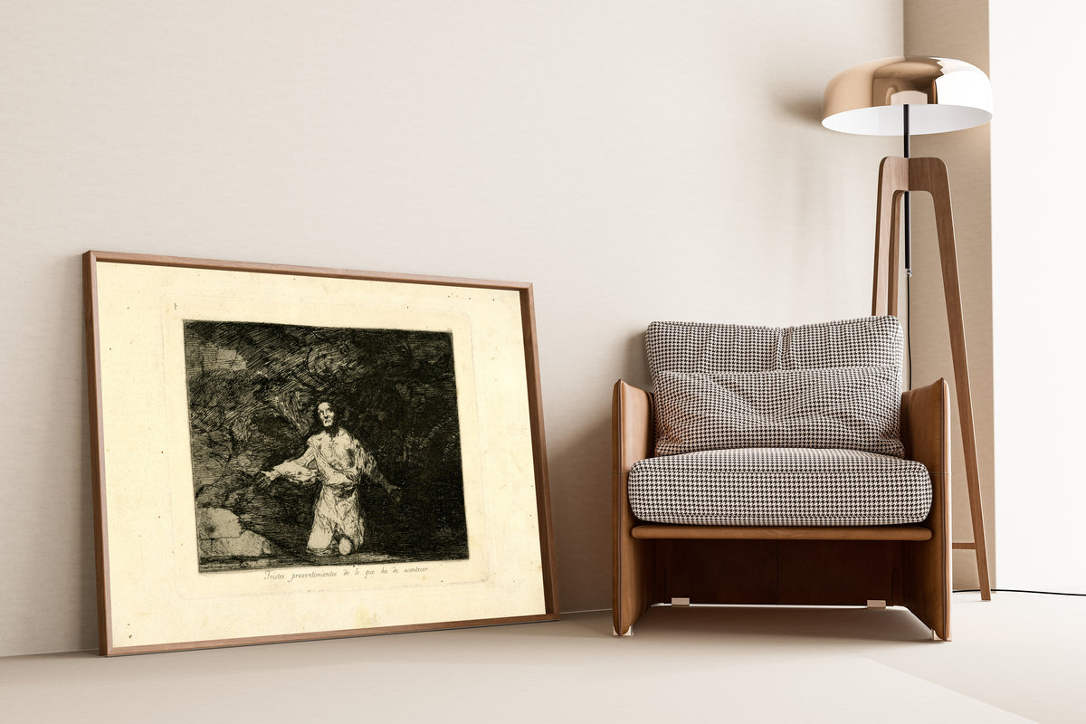 Framed art print of Tristes presentimientos de lo que ha de acontecer (Sad… by Francisco de Goya, leaning against a wall beside an armchair and a floor lamp