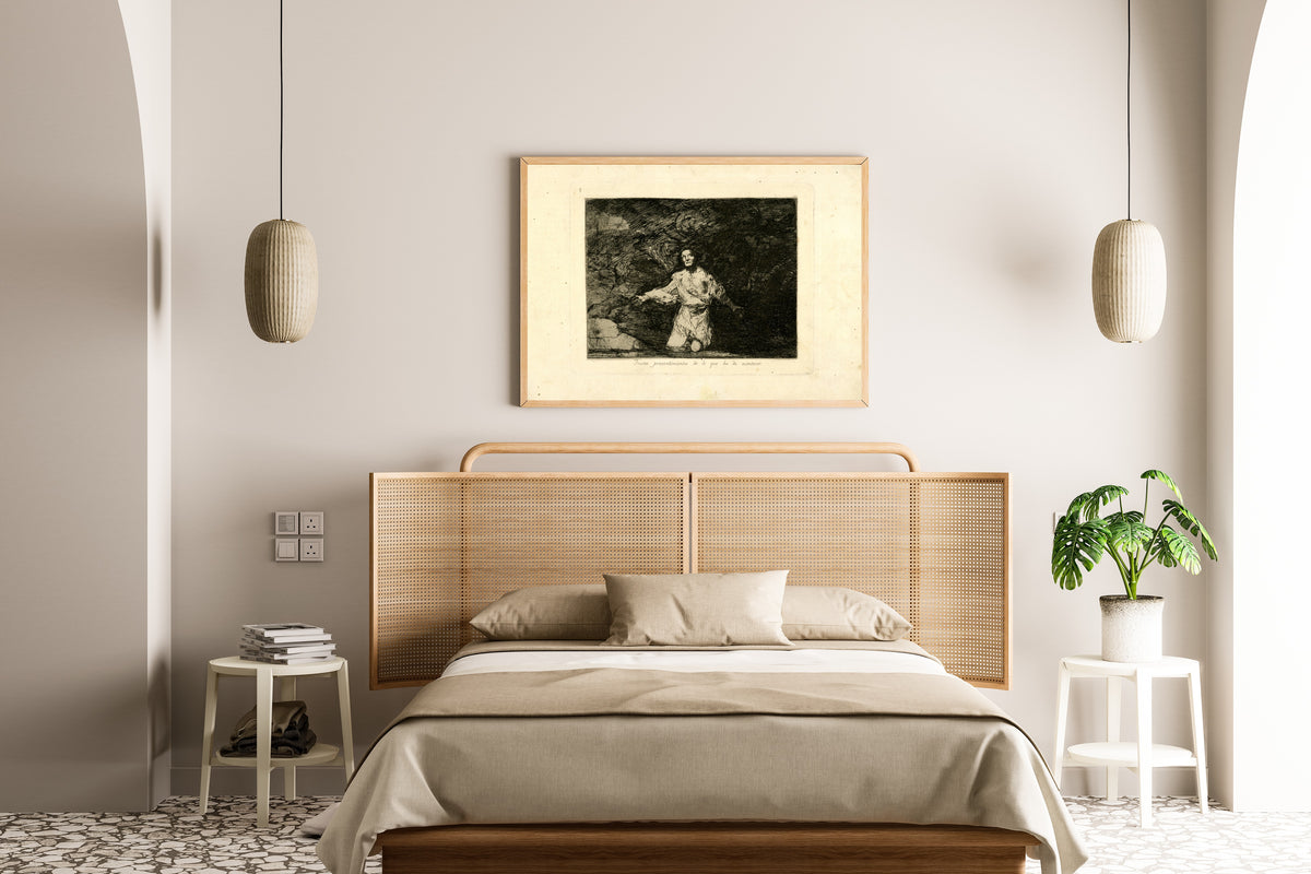 Framed art print of Tristes presentimientos de lo que ha de acontecer (Sad Forebodings of What Is Going to… by Francisco de Goya, above a cane-headboard bed