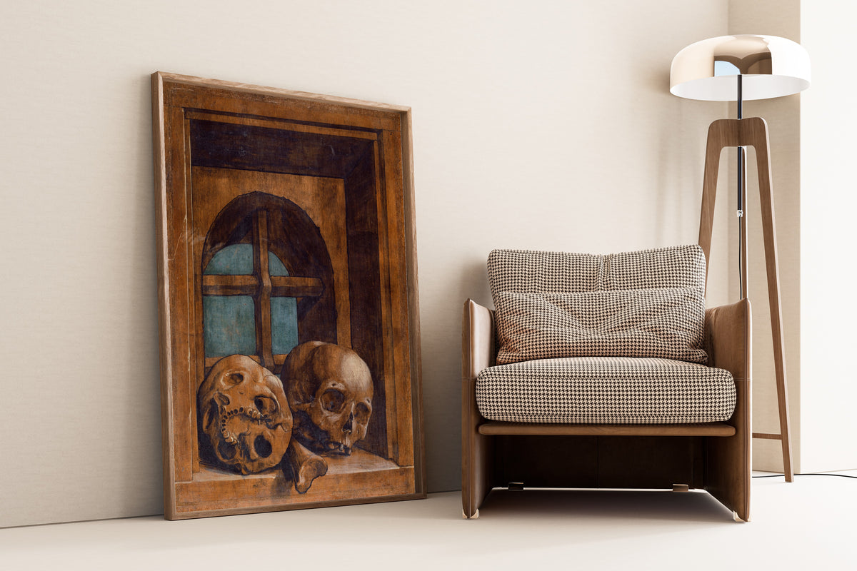 Framed art print of Two Skulls in a Window Niche by Hans Holbein the Younger, leaning against a wall beside an armchair and a floor lamp