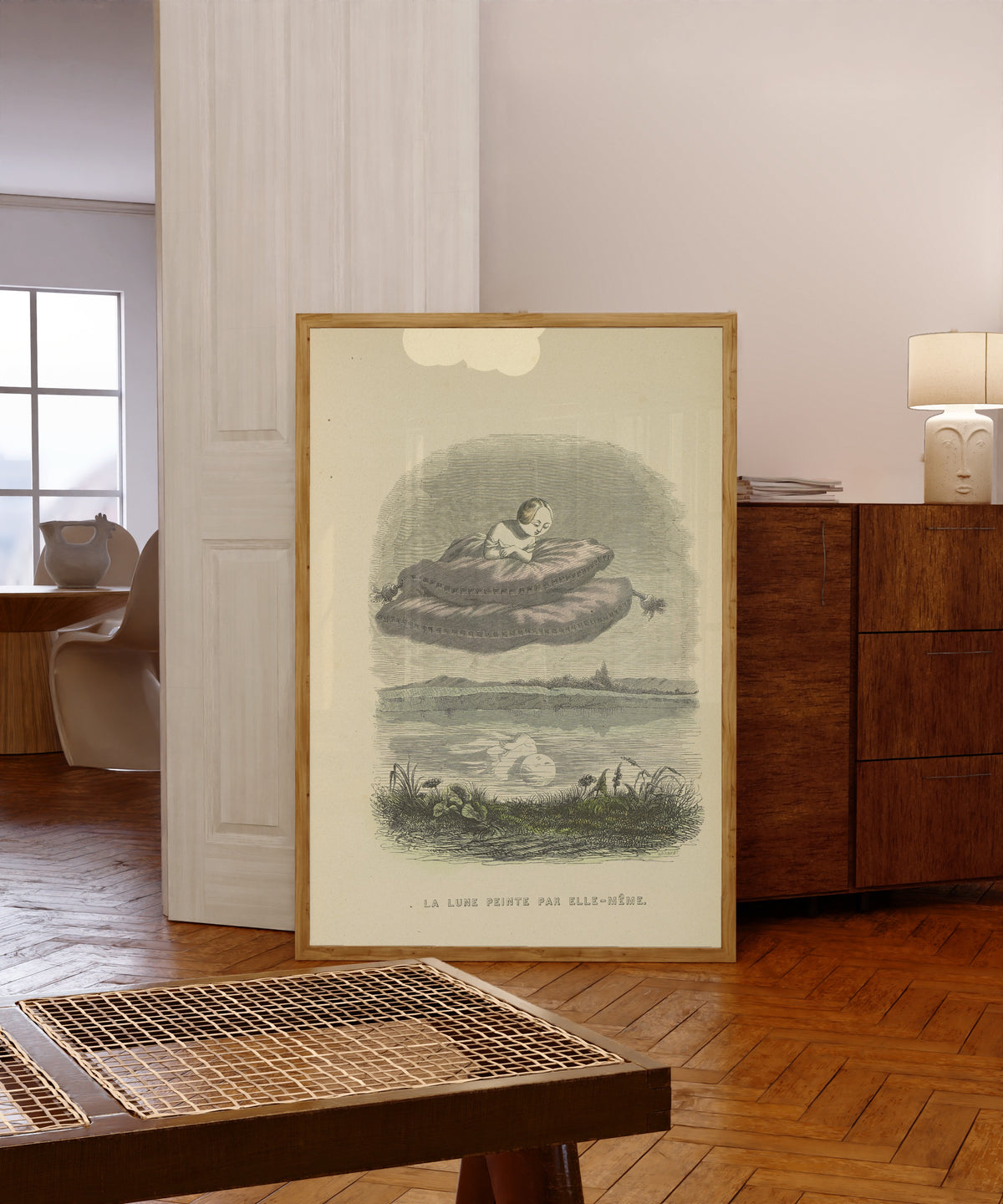 Framed art print of Un autre monde: The Moon Painted by Herself by J. J. Grandville, in a light wood frame leaning in a warm room with a parquet floor