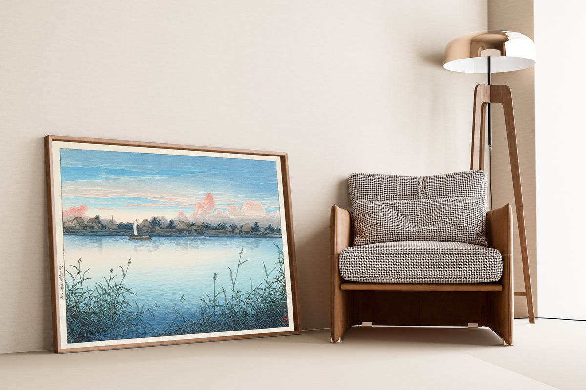 Framed art print of Urayasu in Early Autumn by Kawase Hasui, leaning against a wall beside an armchair and a floor lamp